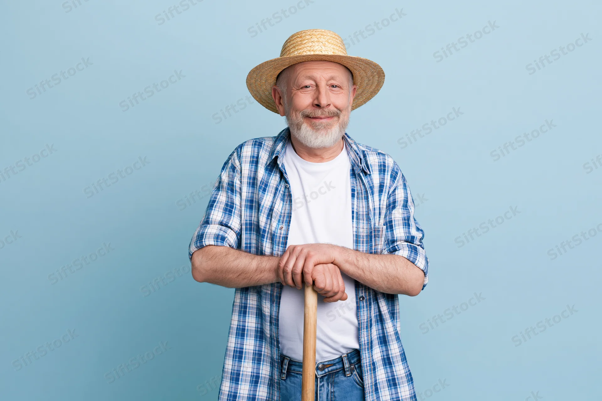 Senior man in straw hat and plaid shirt holding walking stick against blue background