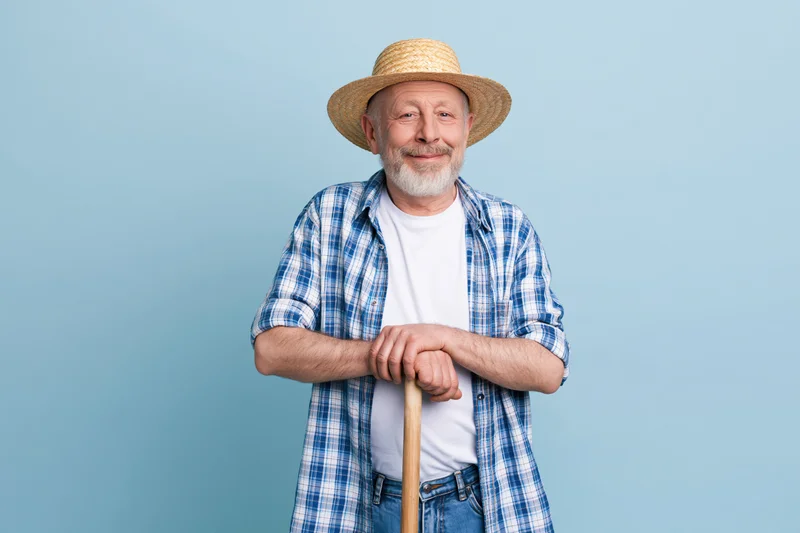 Senior man in straw hat and plaid shirt holding walking stick against blue background