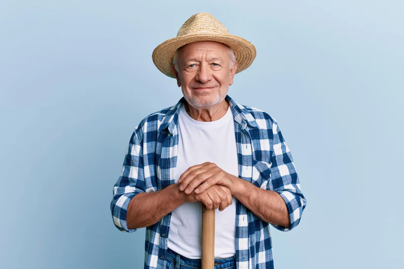 Senior man smiling while holding a wooden cane against a light blue background