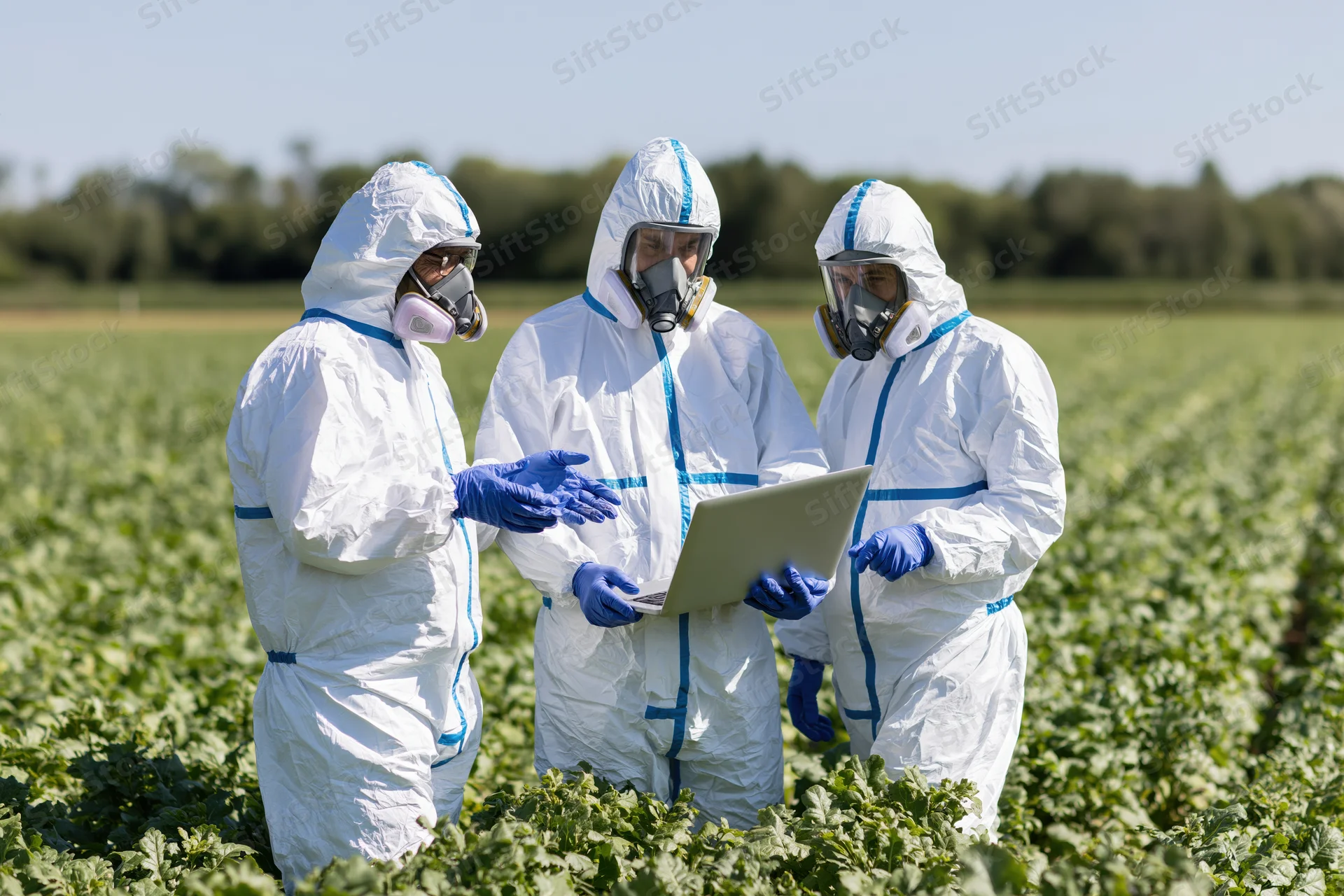 Three scientists in hazmat suits discussing crop data on a laptop in a field