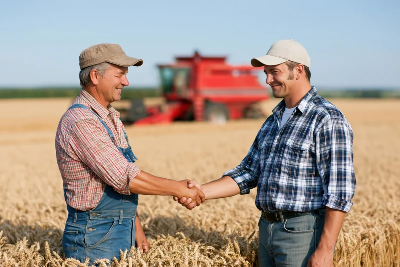Two farmers shaking hands in a wheat field with a red combine harvester in the background