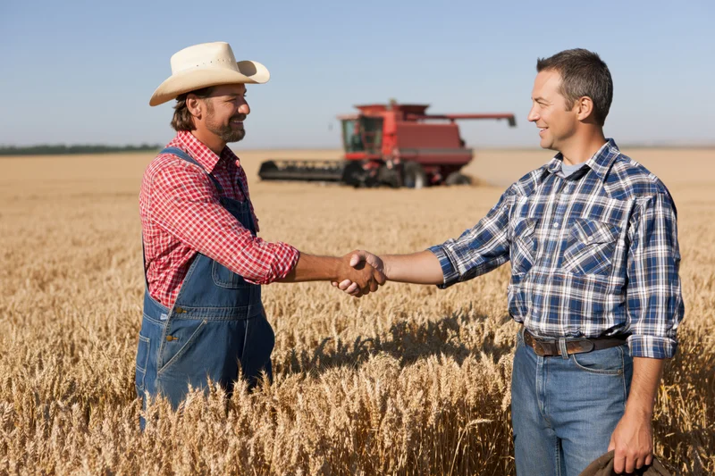 Two farmers shaking hands in a wheat field with a combine harvester in the background