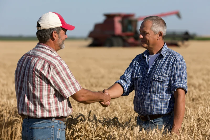 Two farmers shaking hands in a wheat field with a combine harvester in the background