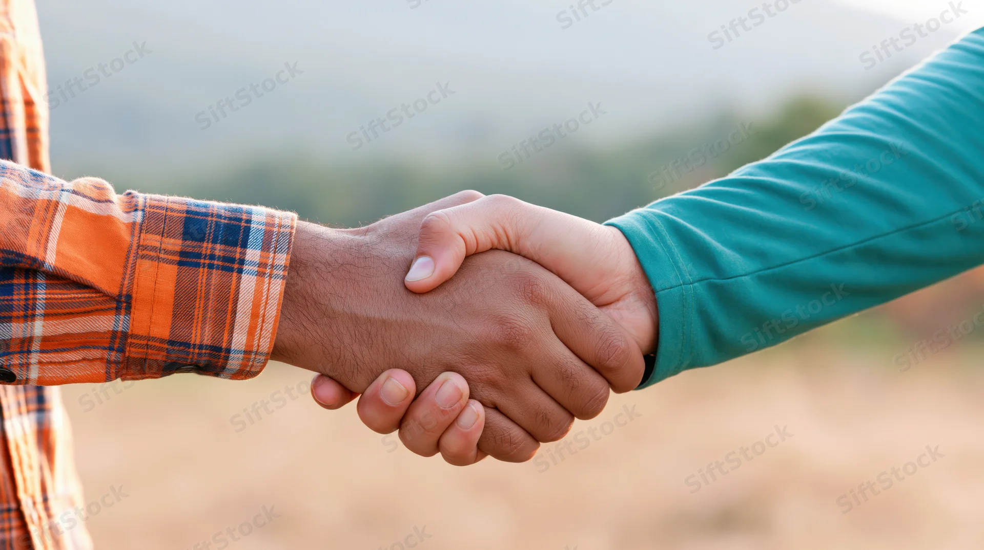 Two hands shaking firmly in an outdoor field setting