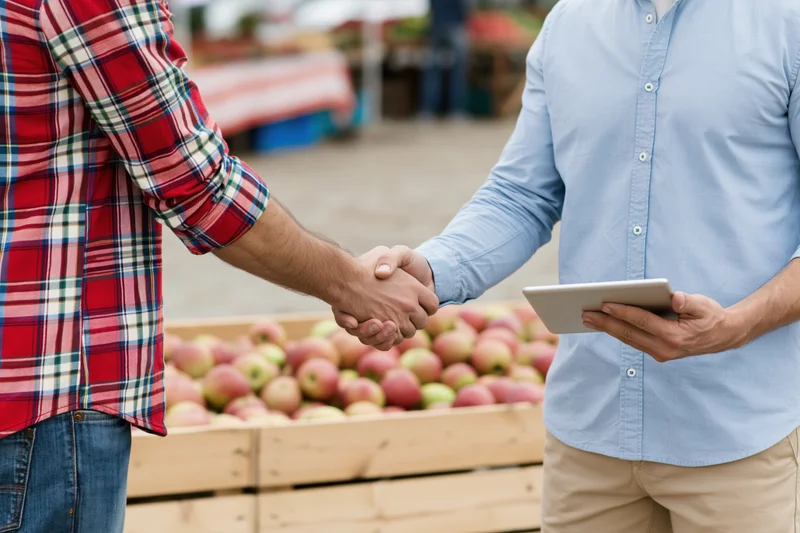 Two men shaking hands over a crate of apples at an outdoor farm market