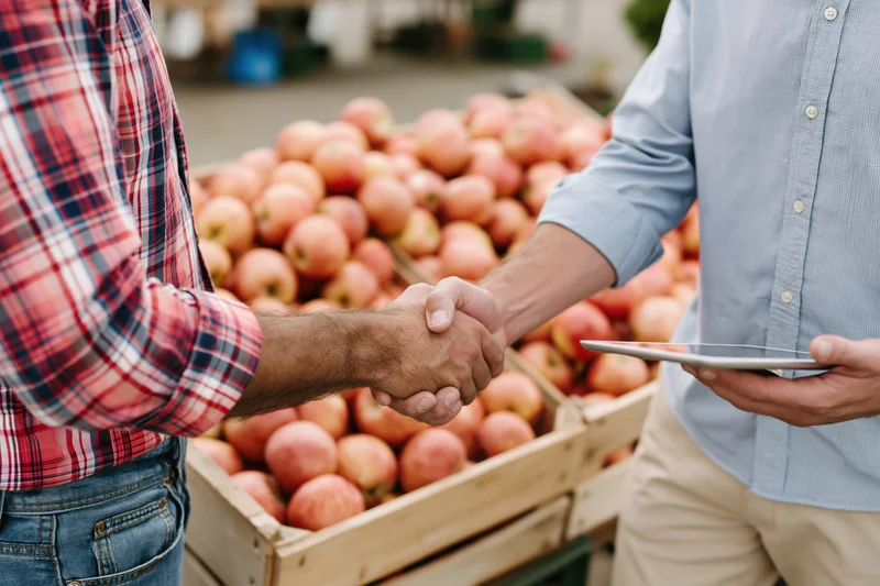 Two men shaking hands over crates of apples at a farm market