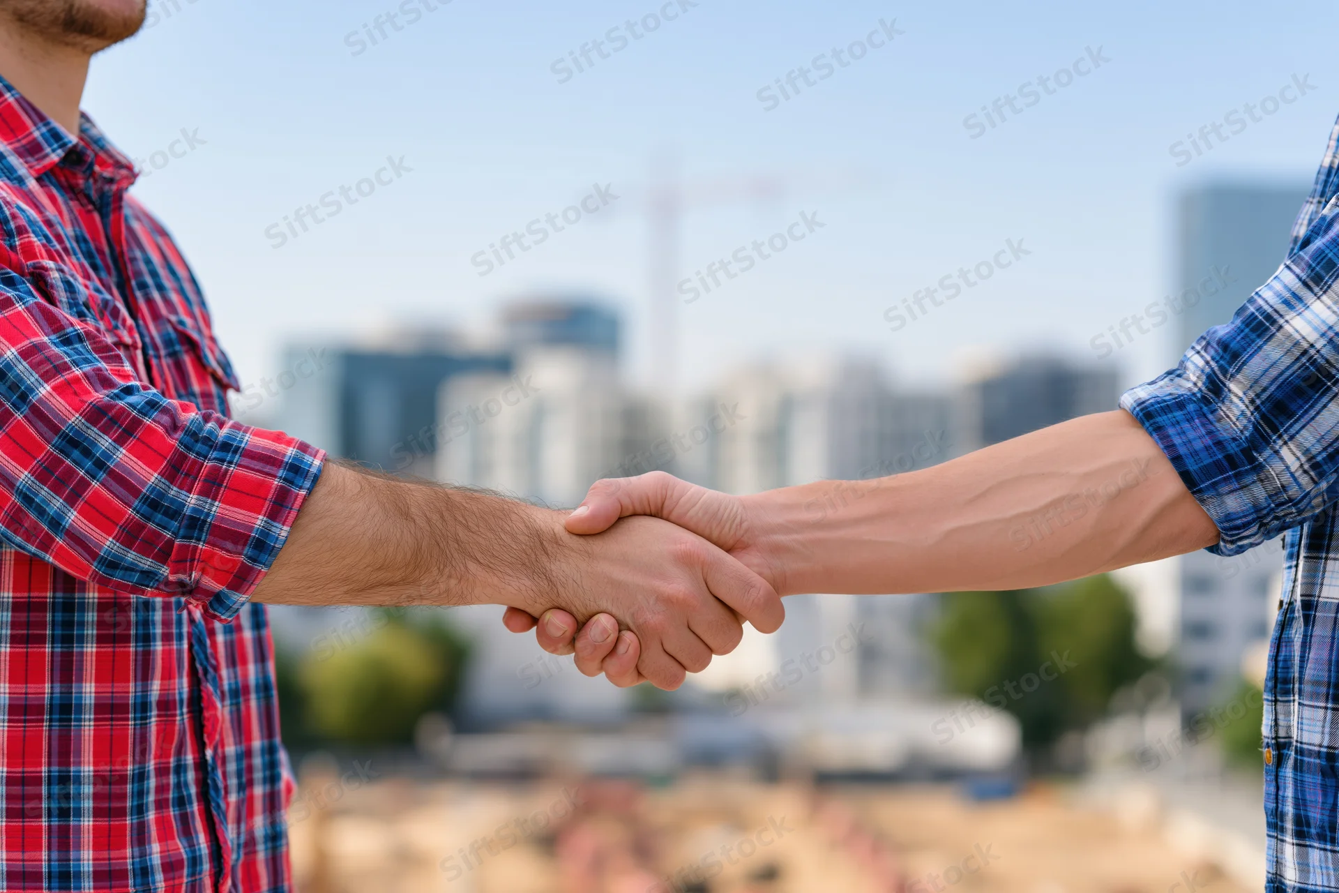 Two men shaking hands at a construction site with city skyline in background