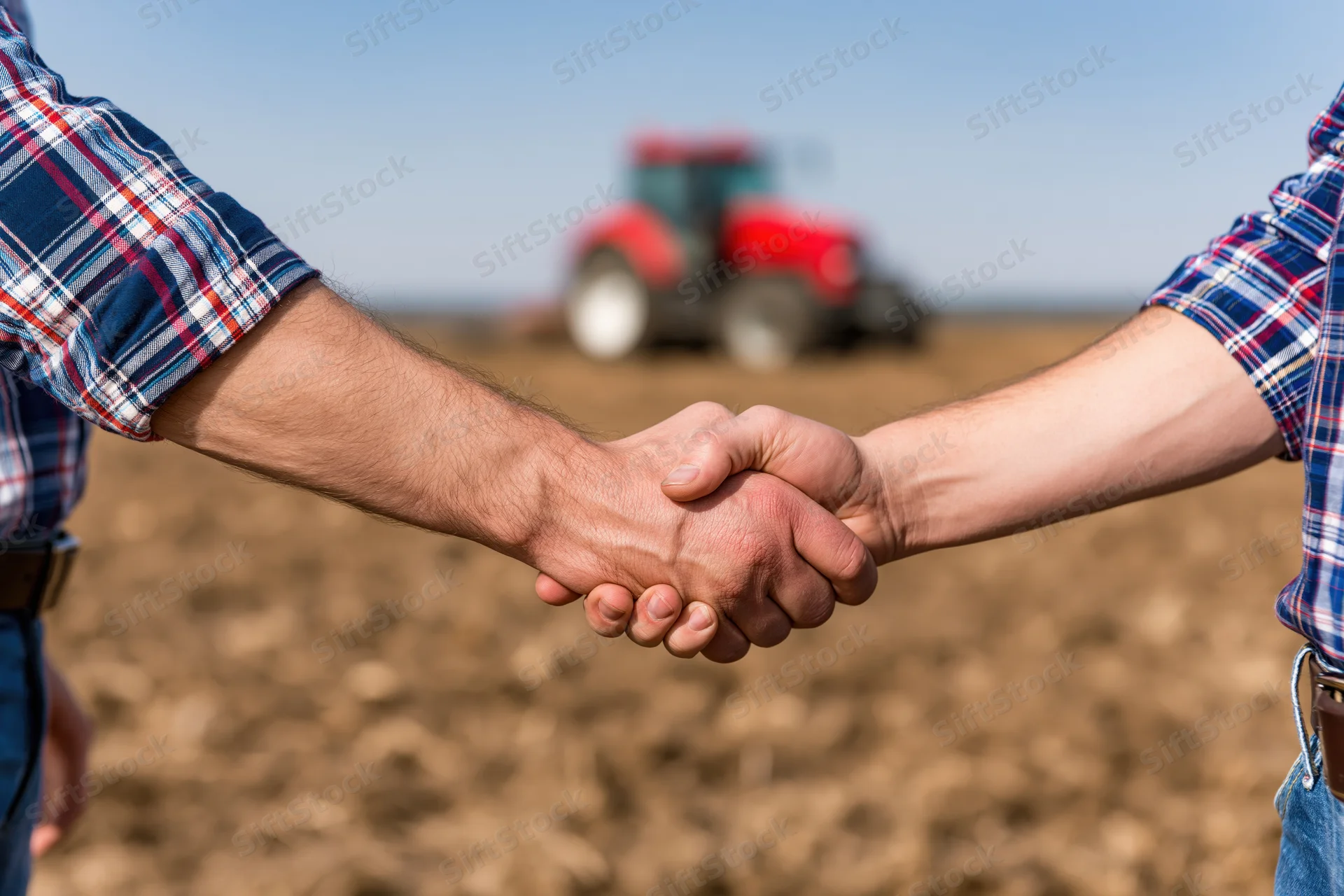 Two farmers shaking hands in a plowed field with a red tractor in the background