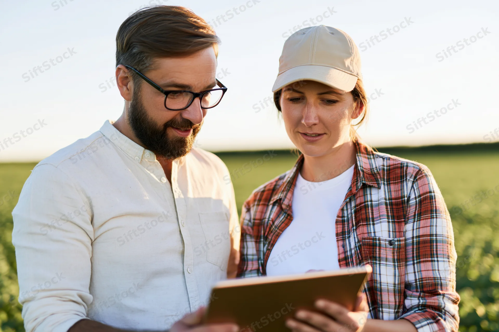 Man and woman examining tablet in a green field during daylight