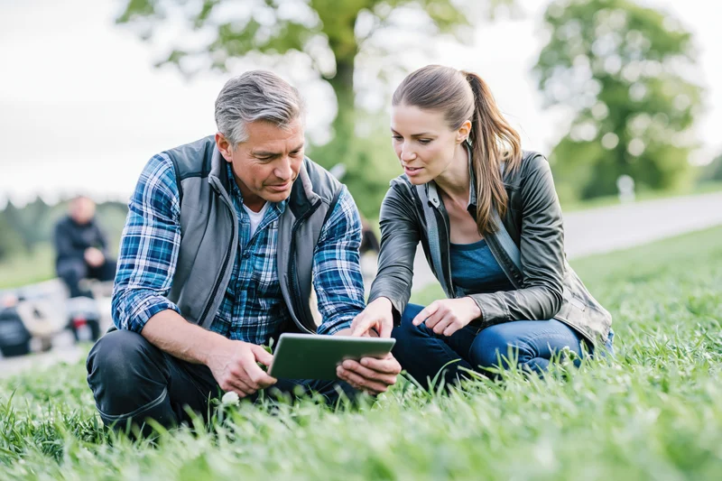 Two researchers crouching on grass examining a tablet together in a park