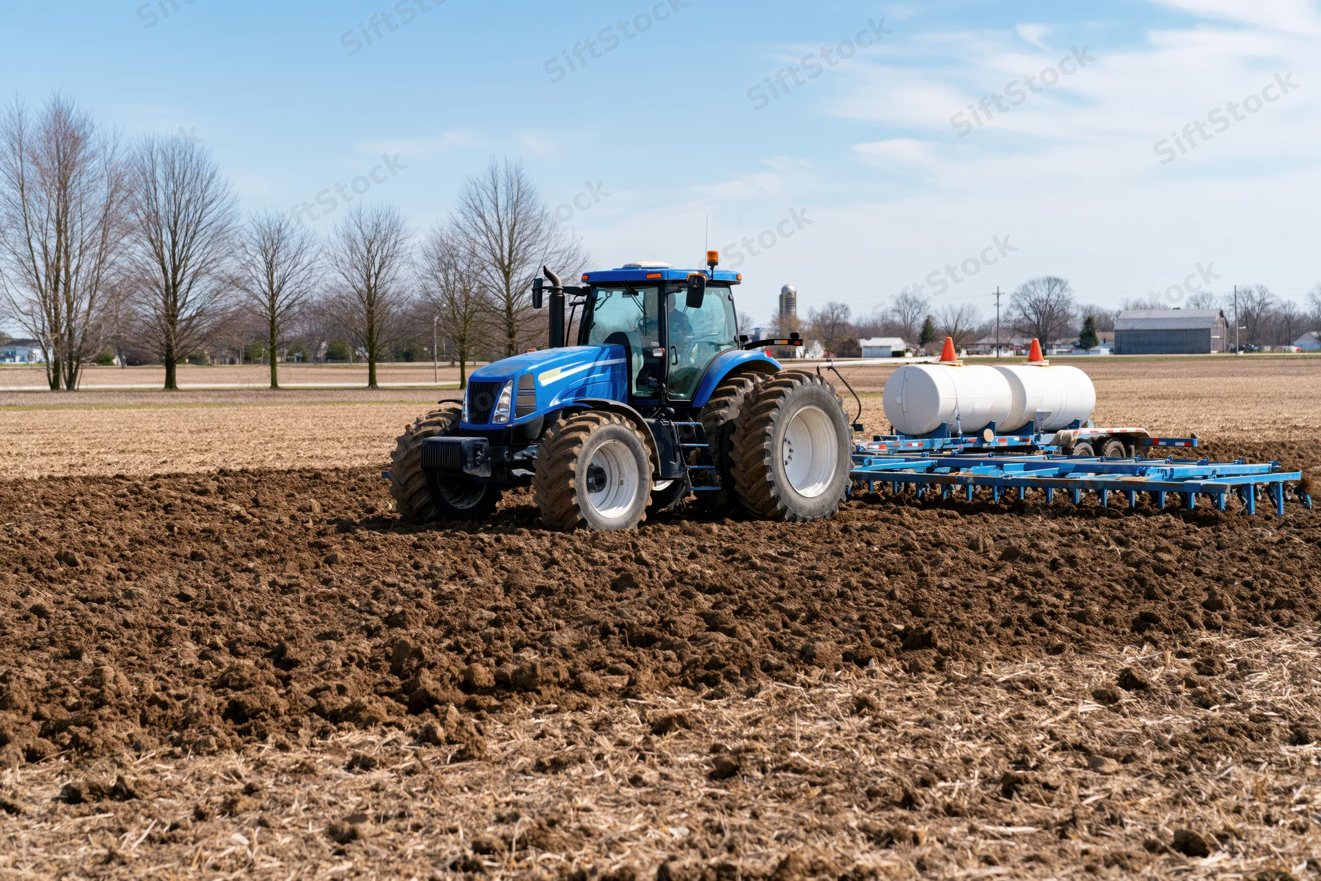 Blue tractor pulls a wide planter across a plowed field