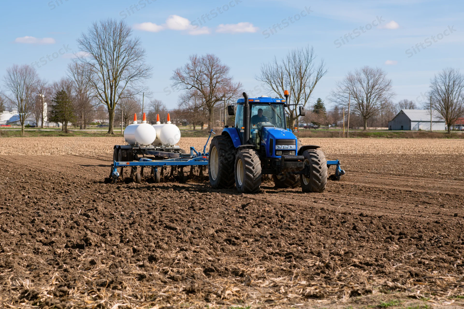 Blue tractor pulling plow across tilled field in rural farmland