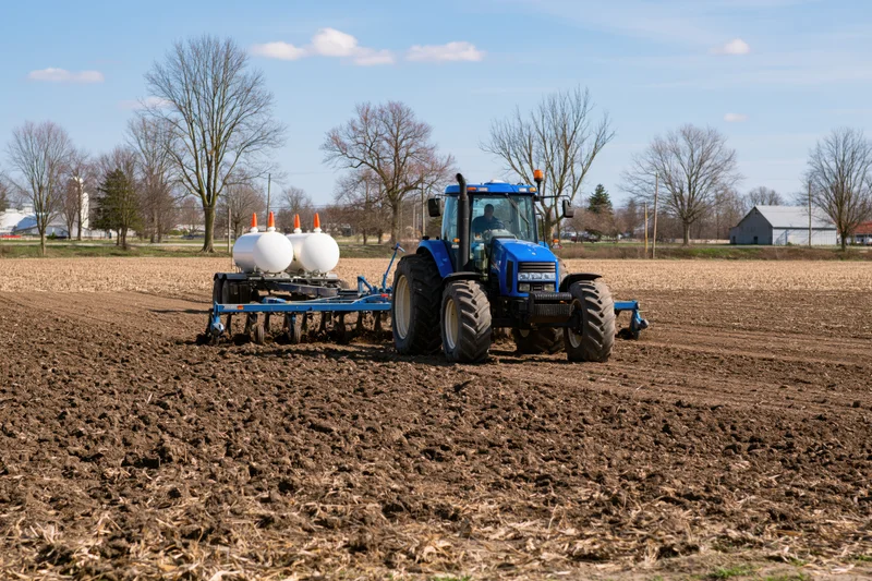 Blue tractor pulling plow across tilled field in rural farmland