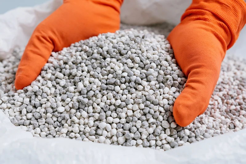Gloved hands holding fertilizer granules from a sack