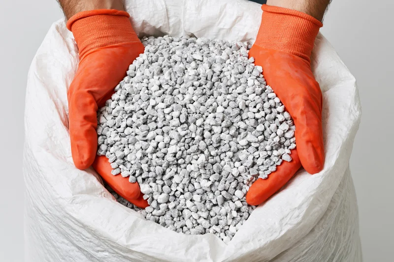 Gloved hands holding gravel from a white bag