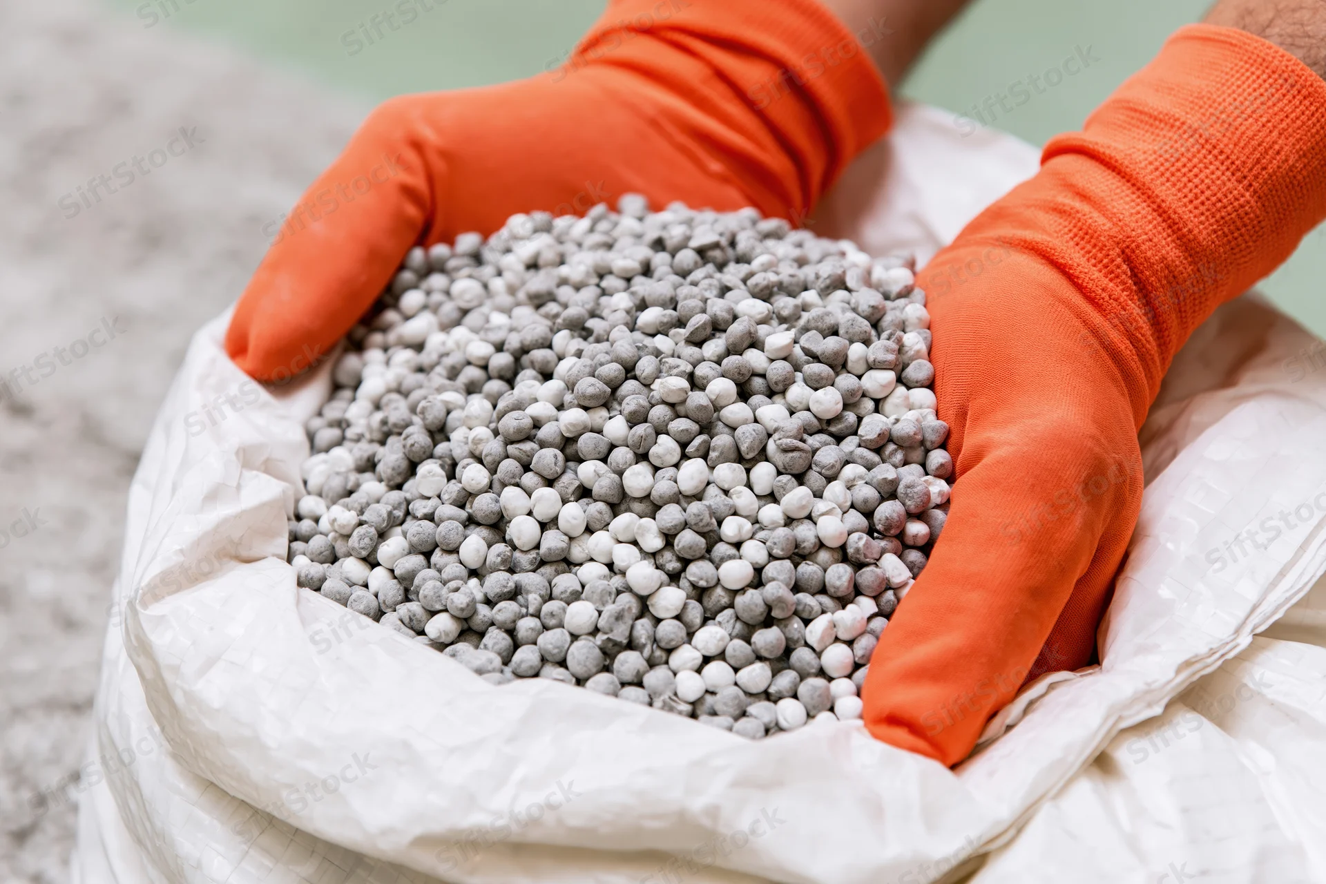 Gloved hands holding granular fertilizer from a white sack