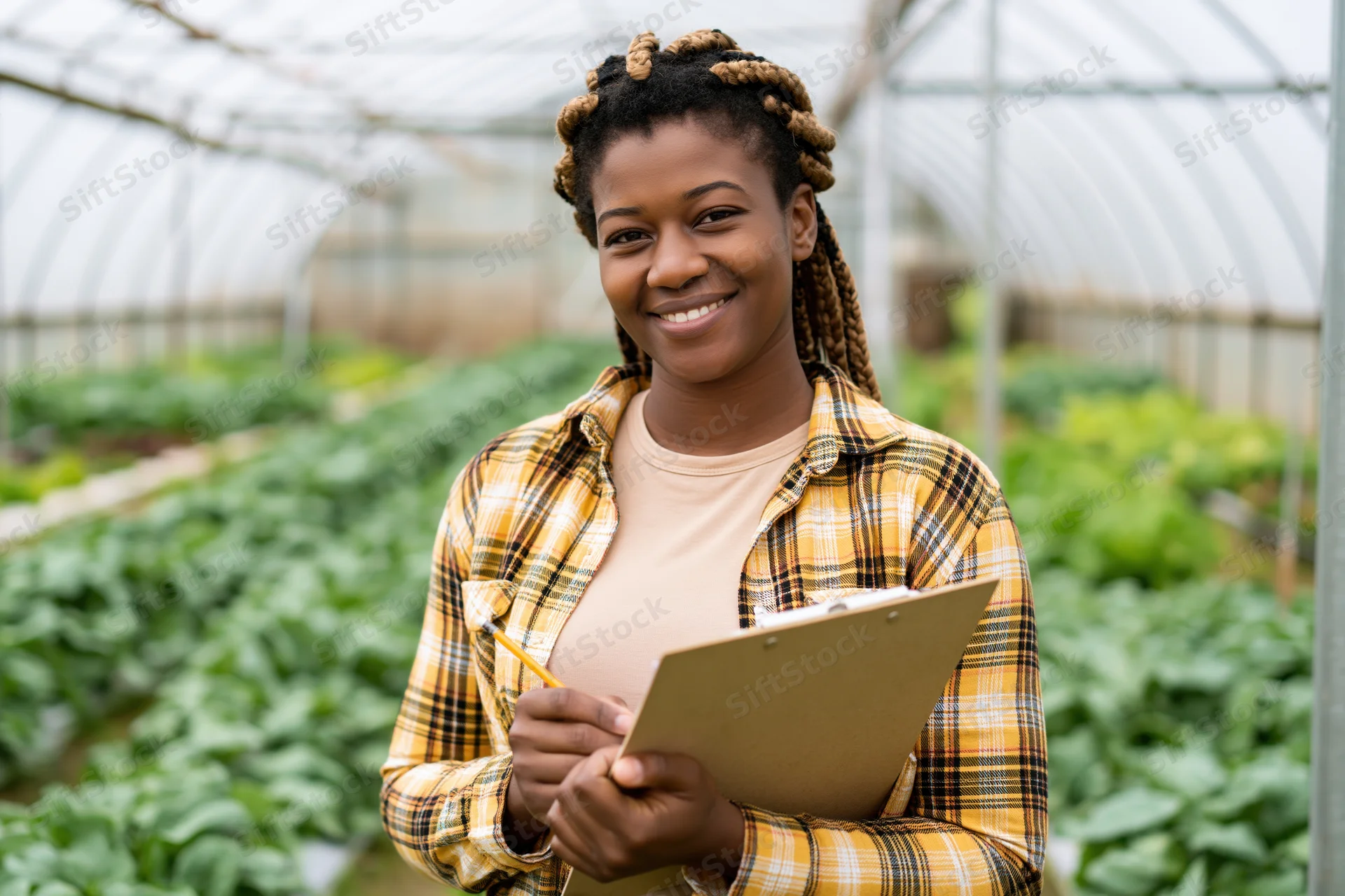 Woman smiling while holding clipboard and pencil in greenhouse garden