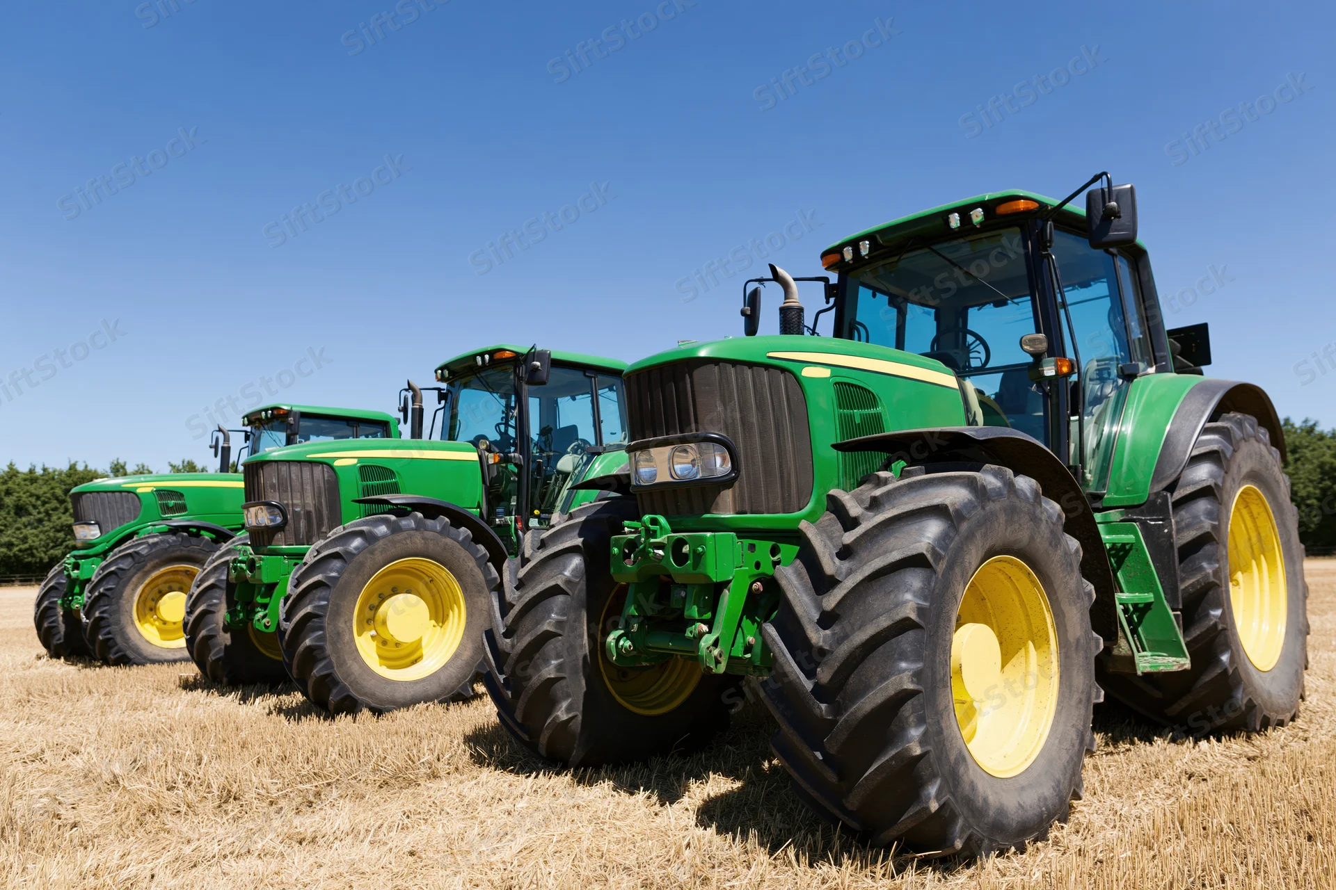Three green and yellow tractors parked in a diagonal row on a dry grass field under a clear blue sky