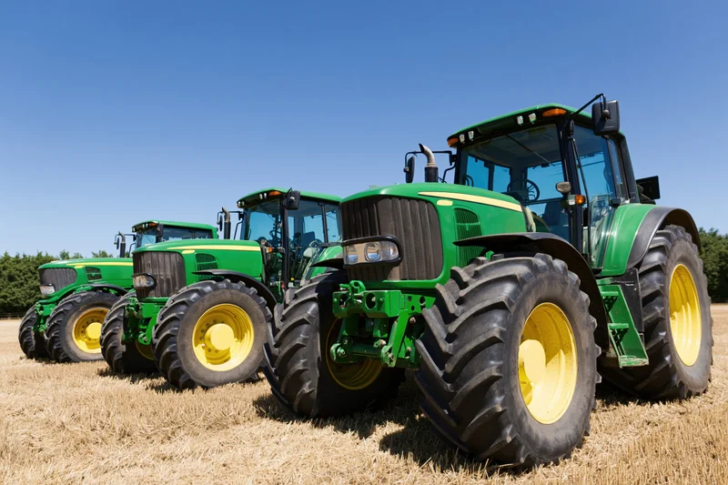 Three green and yellow tractors parked in a diagonal row on a dry grass field under a clear blue sky