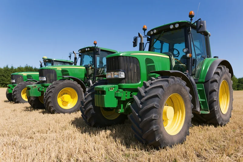 Three green and yellow tractors parked in a diagonal row on a harvested field