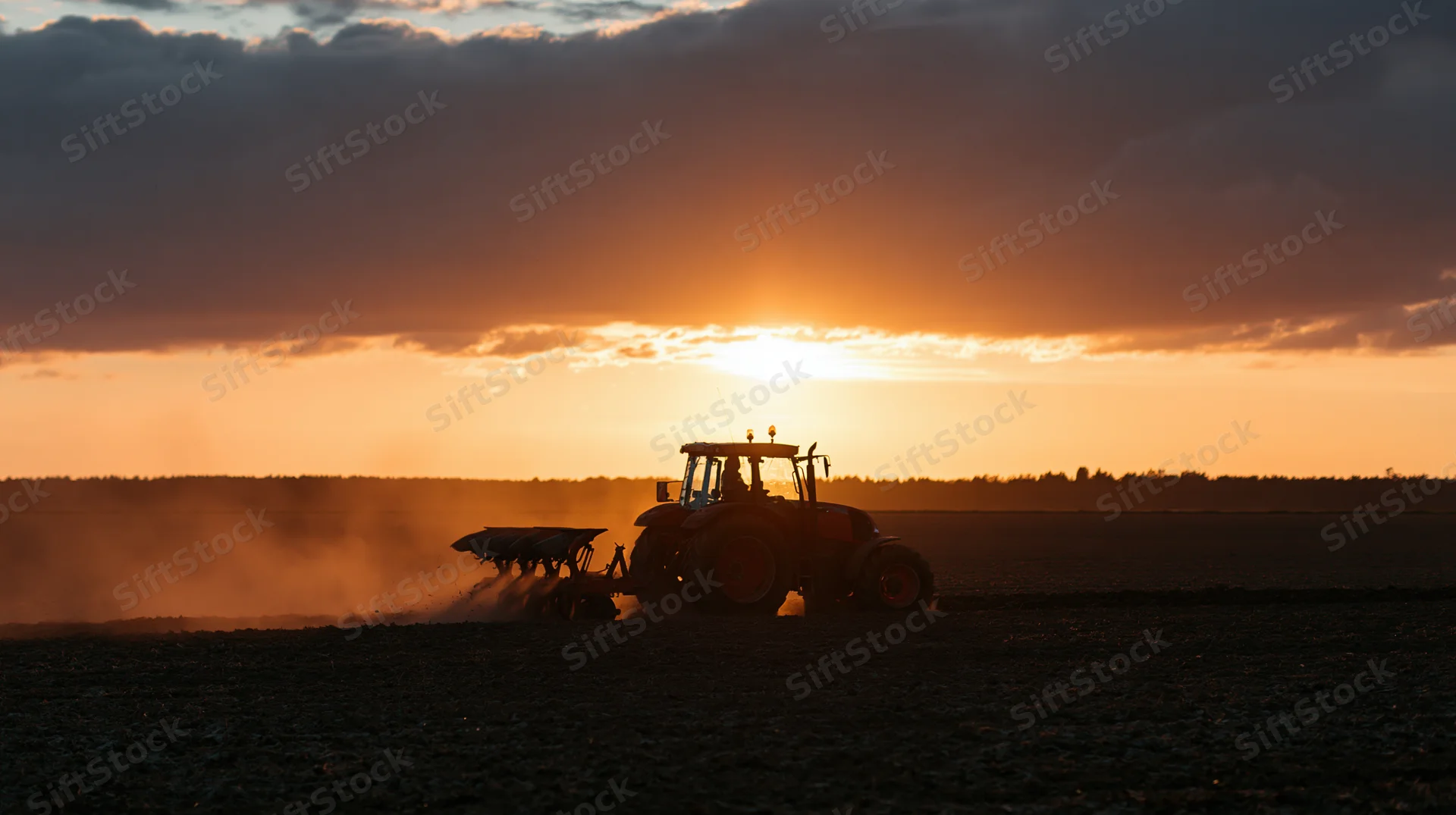 Tractor with attached plow tilling a field at sunset