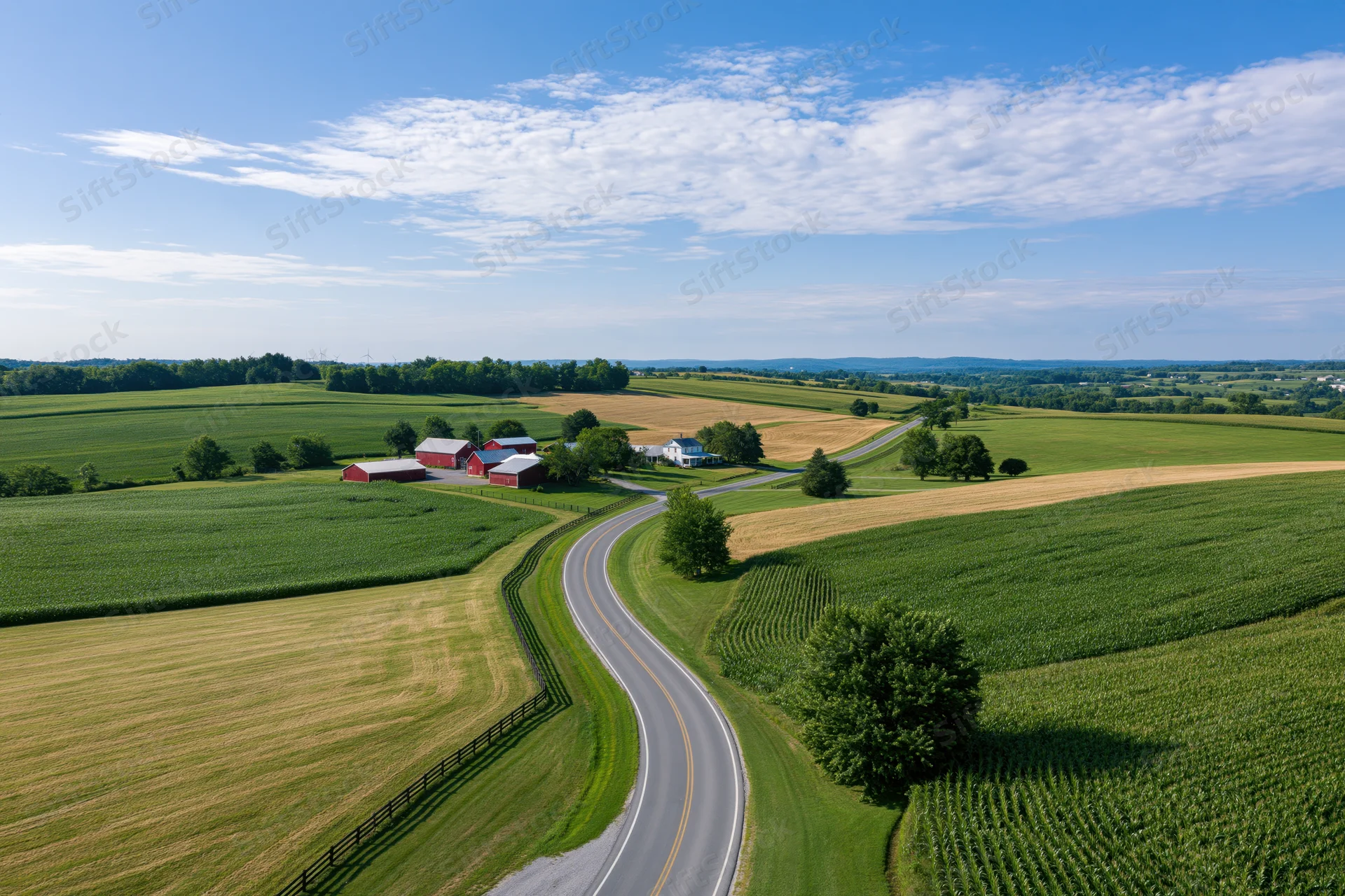 Aerial view of a winding road through green fields and a red barn farm in rural america