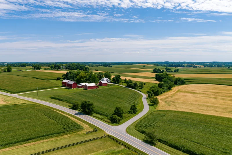 Aerial view of a rural american farm with red barns and cornfields surrounding a road intersection