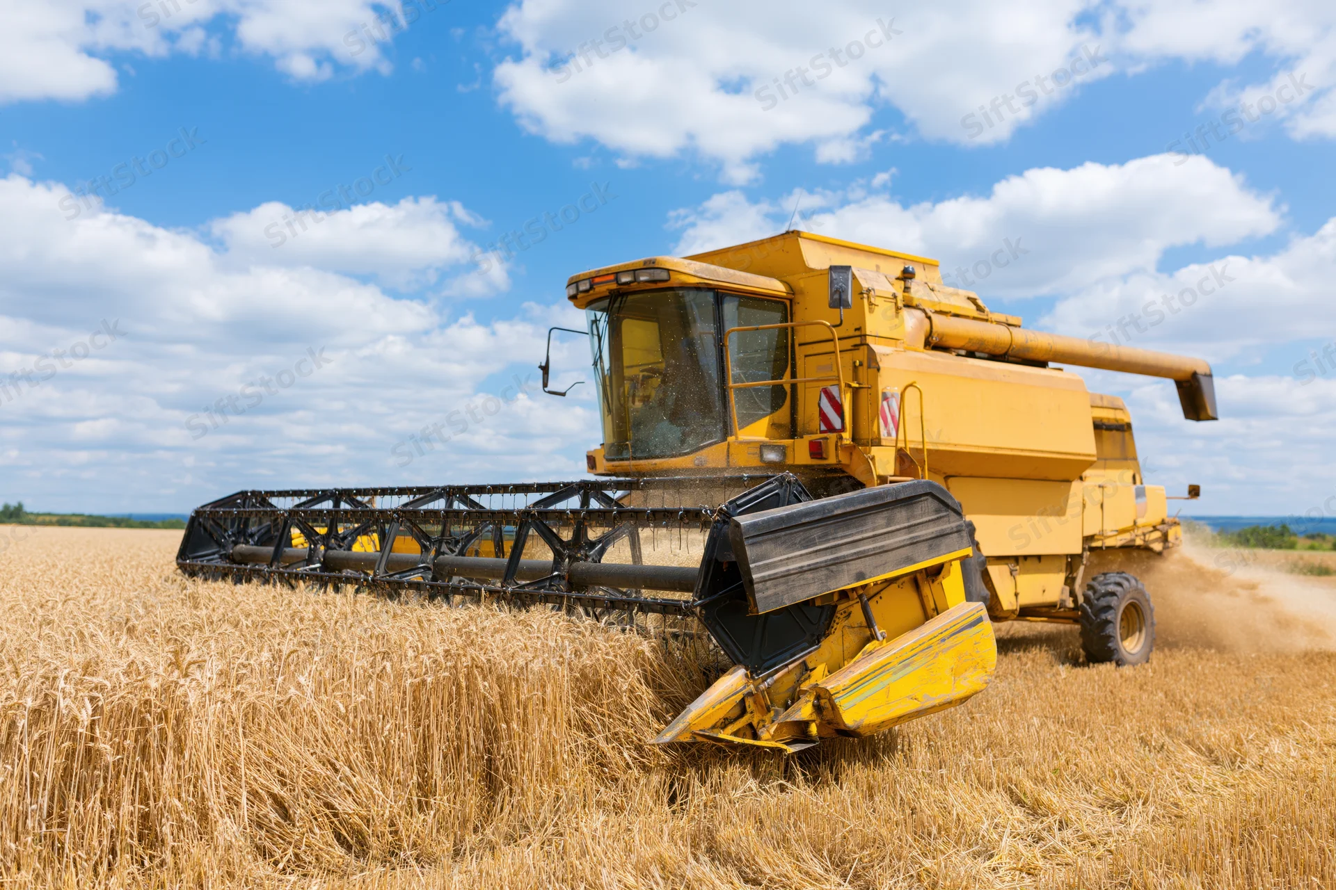 Yellow combine harvester harvesting wheat in a golden field under a blue sky with clouds