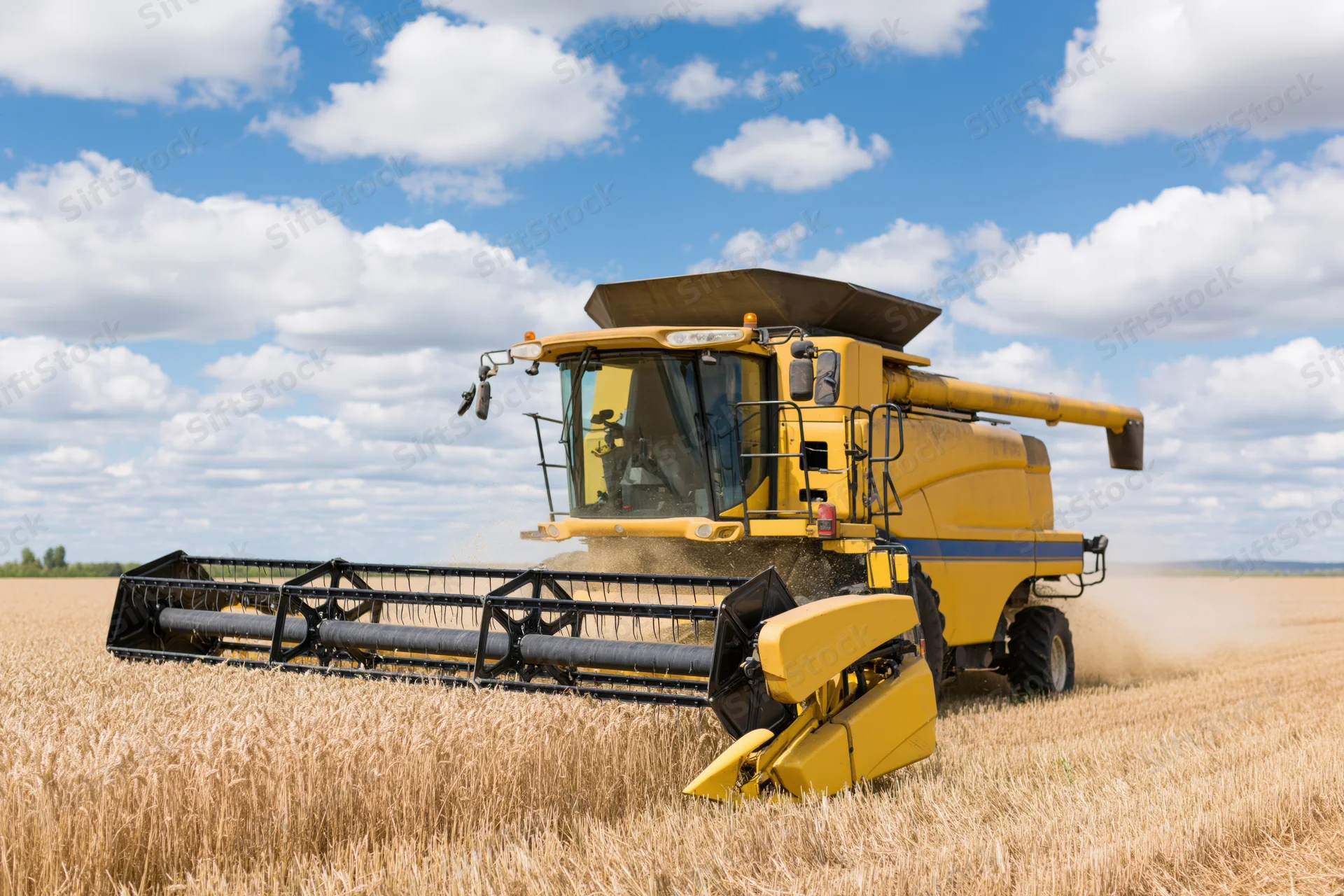 Yellow combine harvester harvesting wheat in a field under a blue sky with clouds