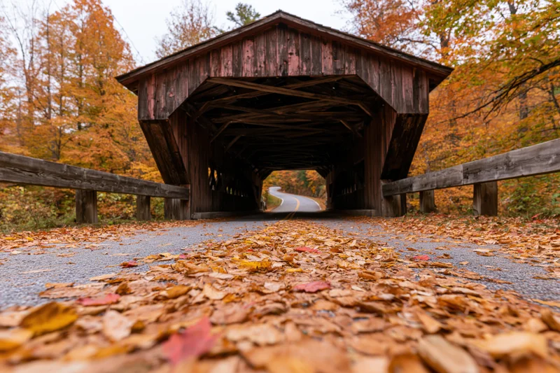 Historic wooden covered bridge over rural road in autumn with fallen leaves on pavement