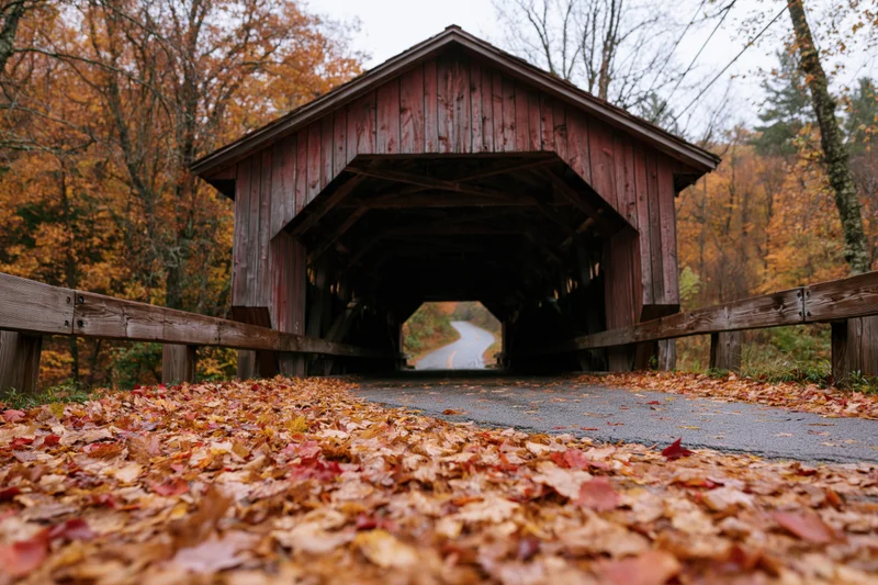 Wooden covered bridge over rural road in autumn with fallen leaves on pavement