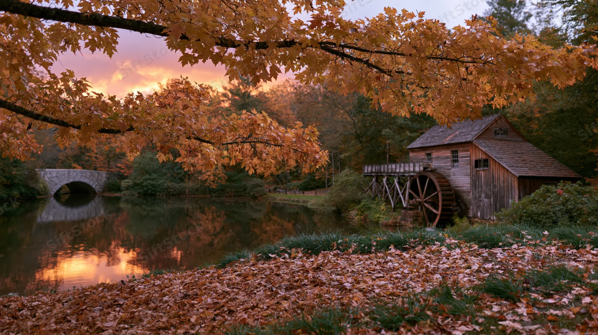 Historic wooden grist mill with large water wheel beside a river at sunset in autumn foliage