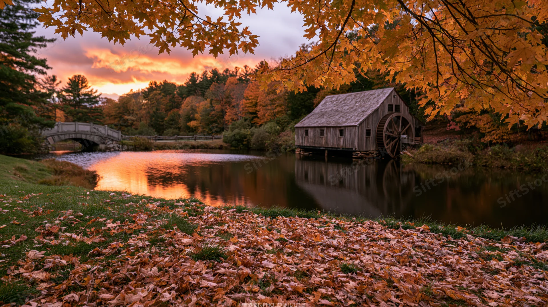 Historic wooden grist mill with large water wheel beside a river at sunset in autumn foliage