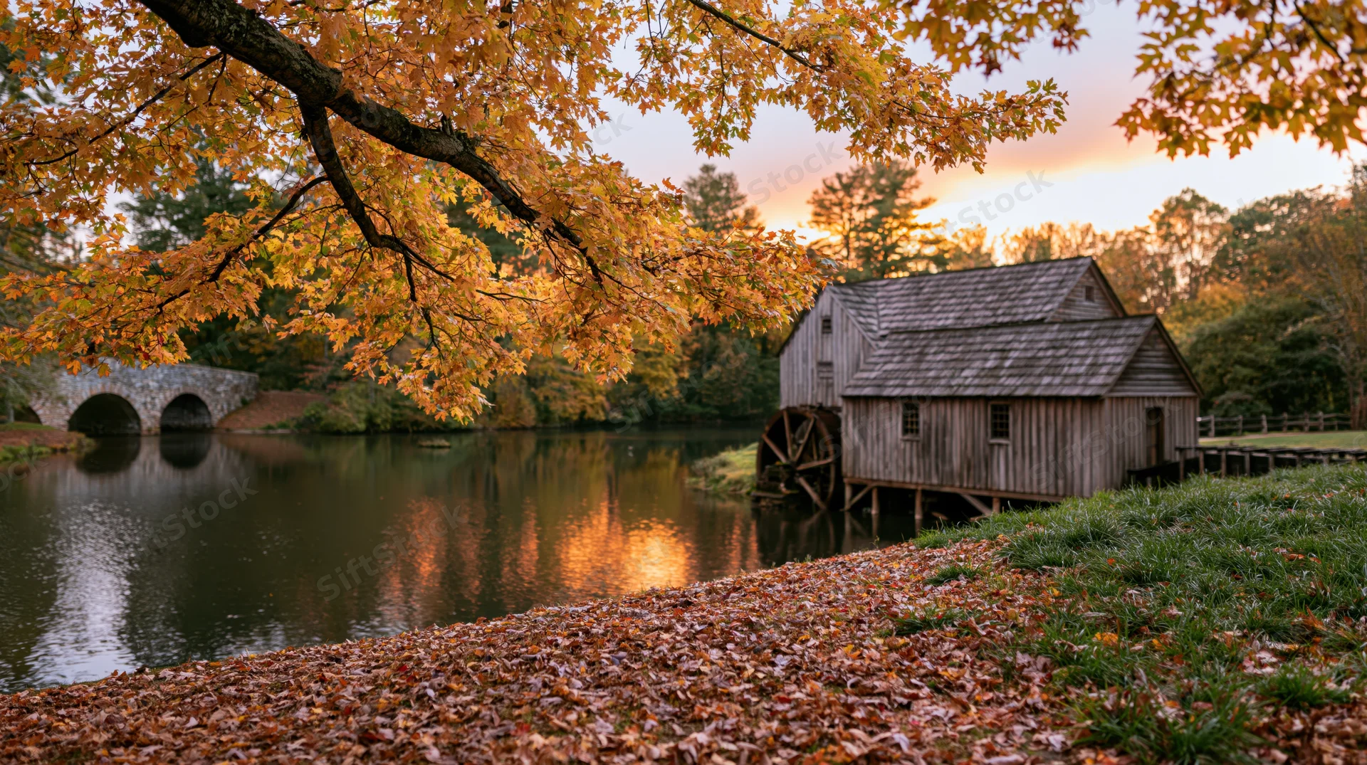 Historic wooden grist mill with waterwheel beside river at sunset in autumn foliage