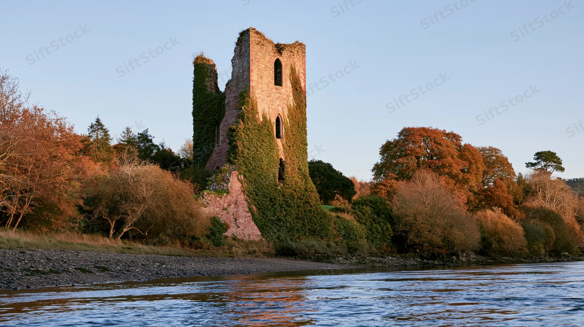 Ivy-covered medieval castle ruin rising above calm river surrounded by autumn trees