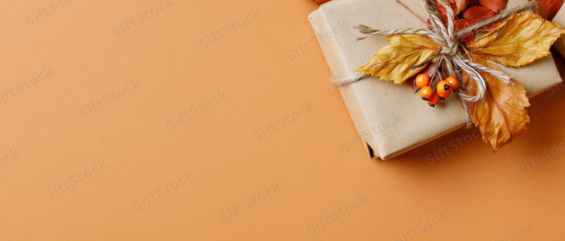 Kraft paper gift box decorated with dried autumn leaves and berries on orange background