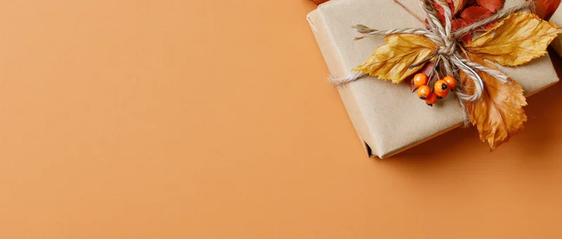 Kraft paper gift box decorated with dried autumn leaves and berries on orange background