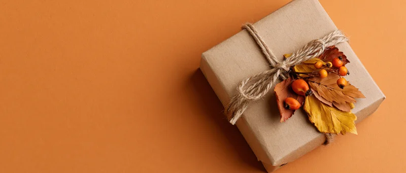 Kraft paper gift box tied with twine and decorated with dried autumn leaves and berries on orange background