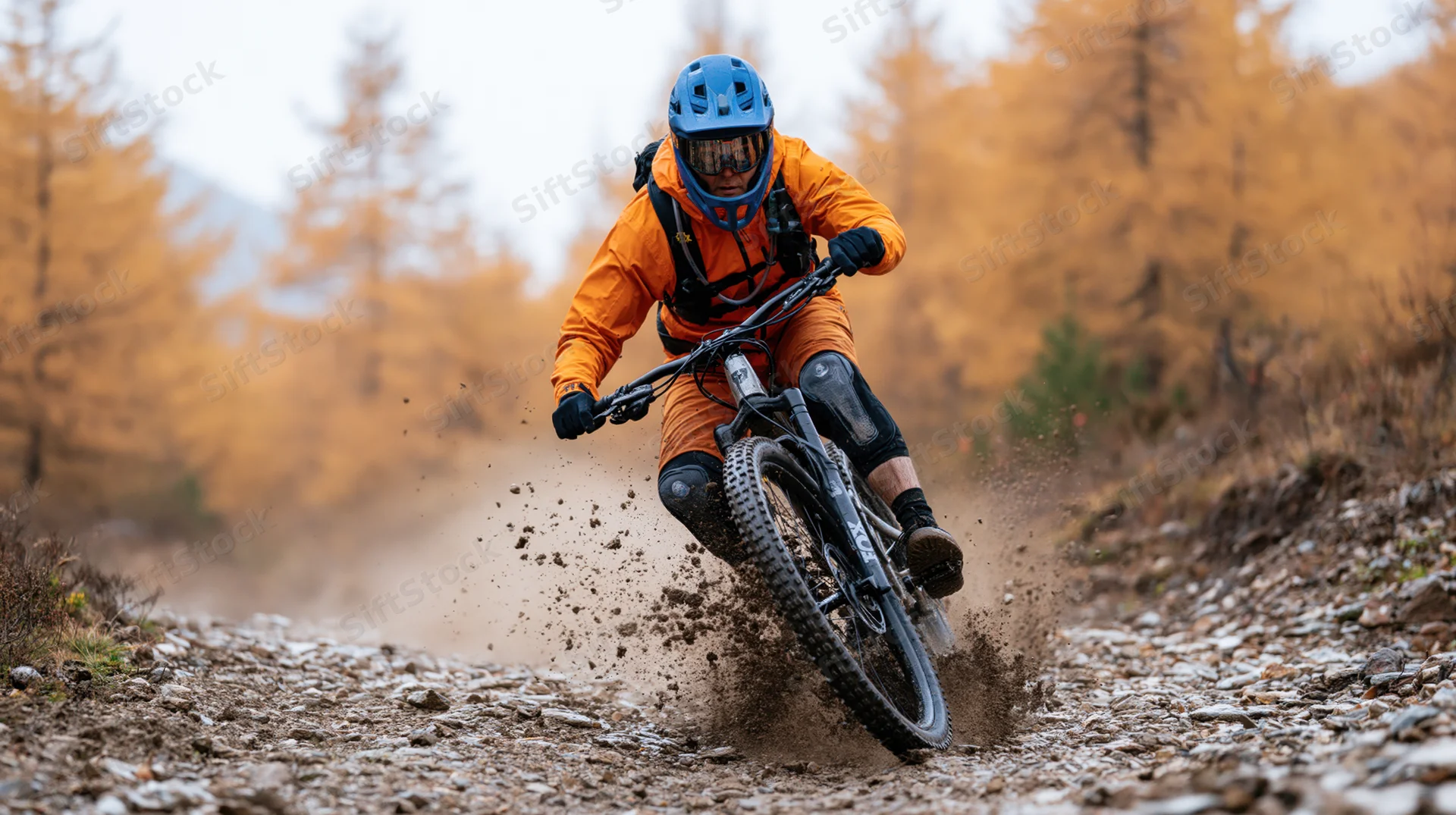 Mountain biker riding downhill on rocky dirt trail through autumn forest