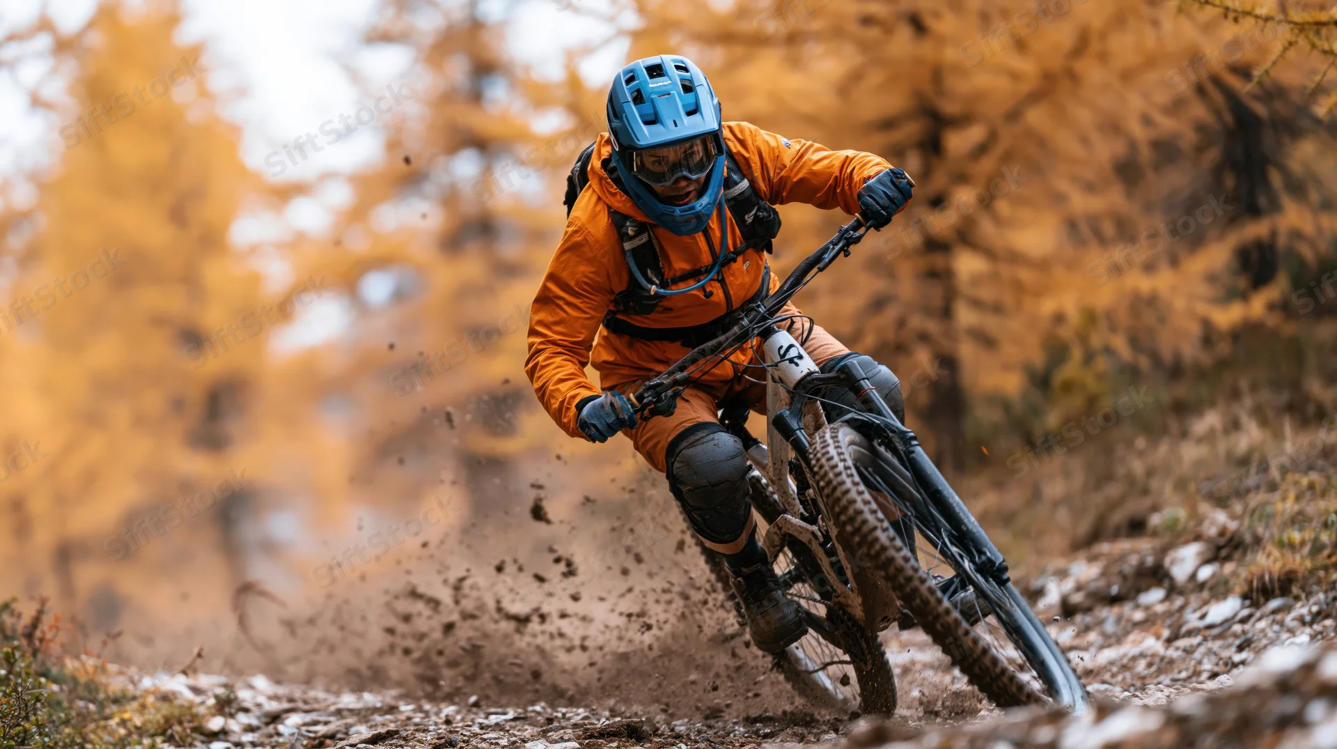 Mountain biker riding downhill on rocky dirt trail in autumn forest