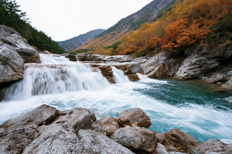Waterfall cascading over granite ledges into a river surrounded by autumn foliage in a mountain valley