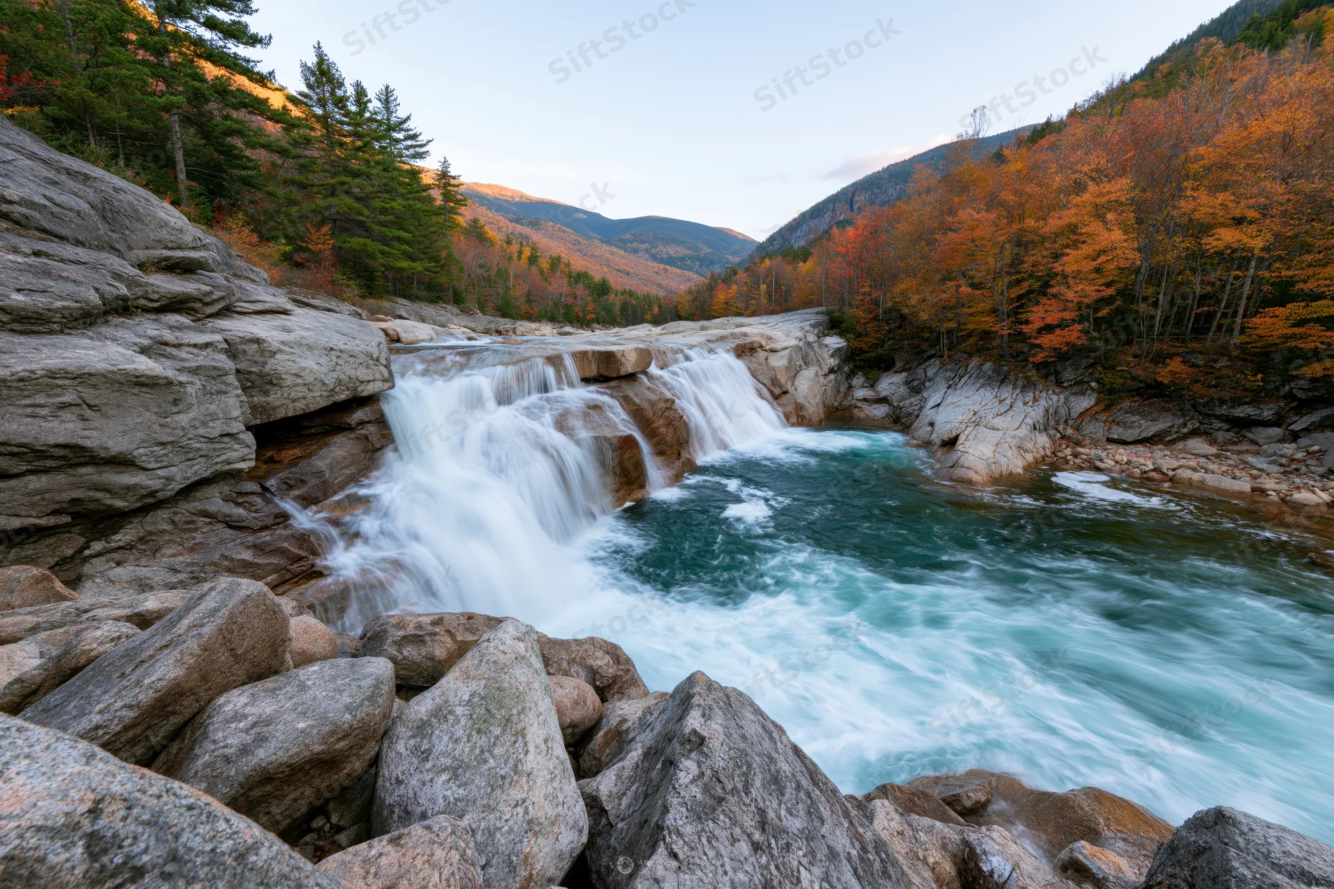 Waterfall cascading over granite ledges into a river surrounded by autumn forest in a mountain valley