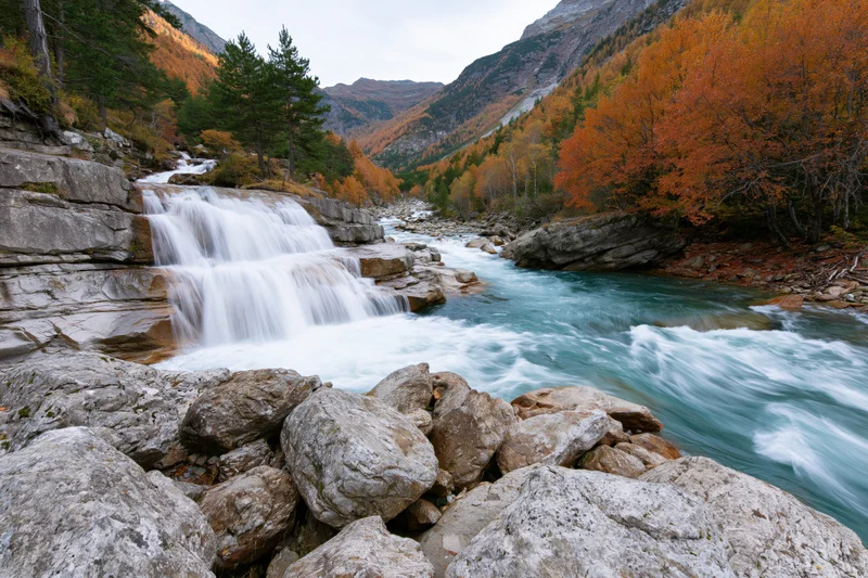 Waterfall cascading over granite ledges into a river in an autumn mountain valley