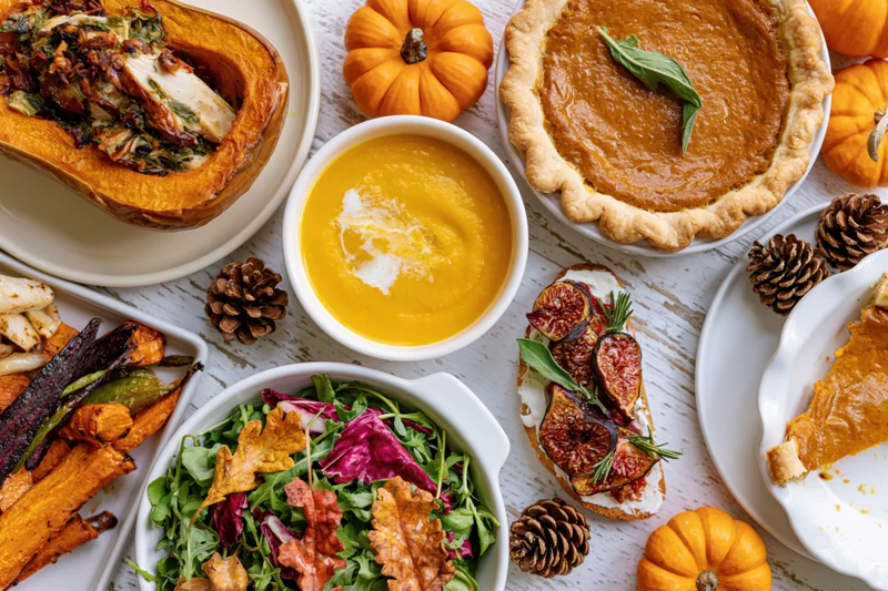 Overhead flat lay of thanksgiving dishes including pumpkin pie, soup, salad, roasted squash and figs on a whitewashed wooden table