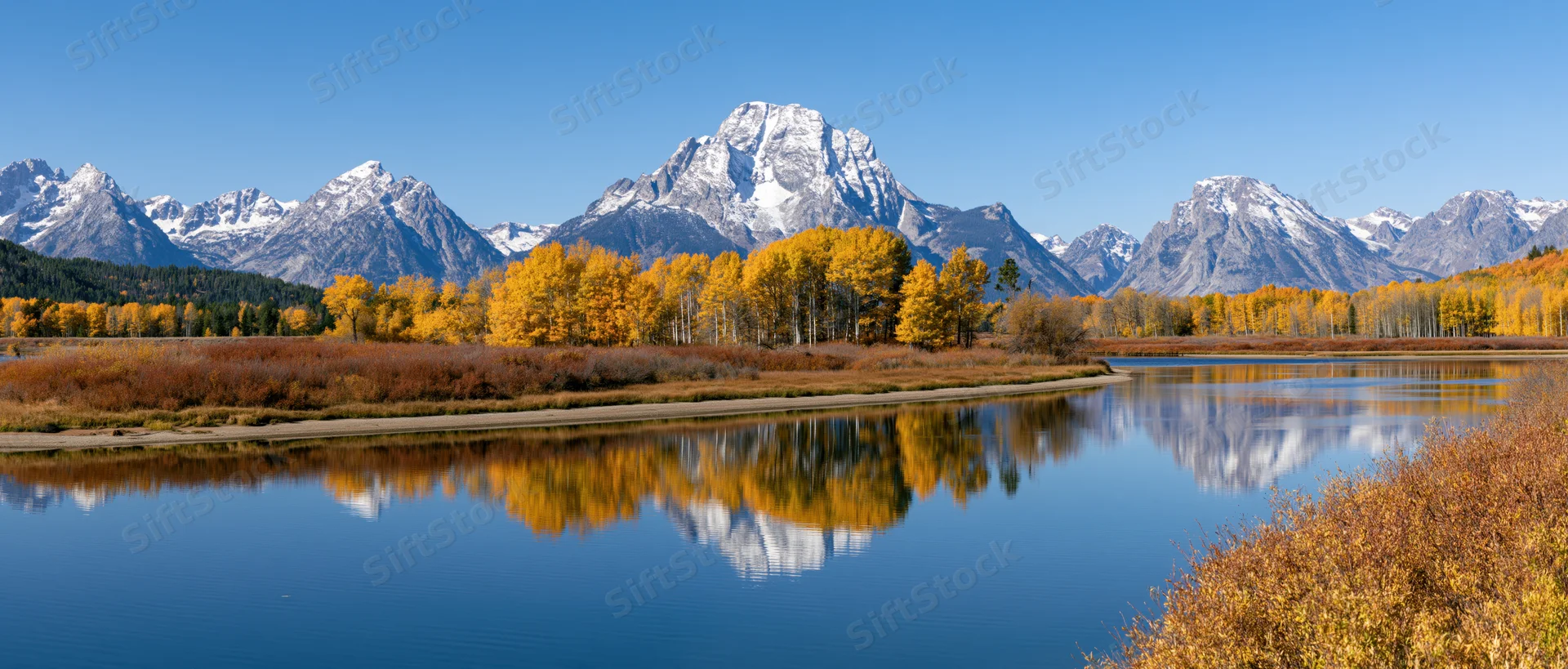 Snow-capped mountains reflected in calm river surrounded by autumn trees at oxbow bend
