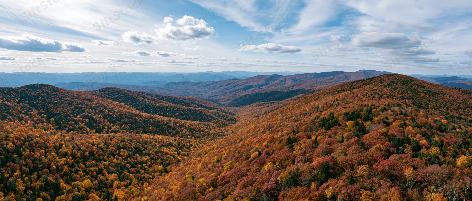 Panoramic view of autumn-colored forested mountains under a partly cloudy sky