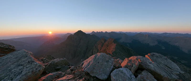 Panoramic view from rocky mountain ridge at sunrise showing jagged peaks and distant valley under dawn sky