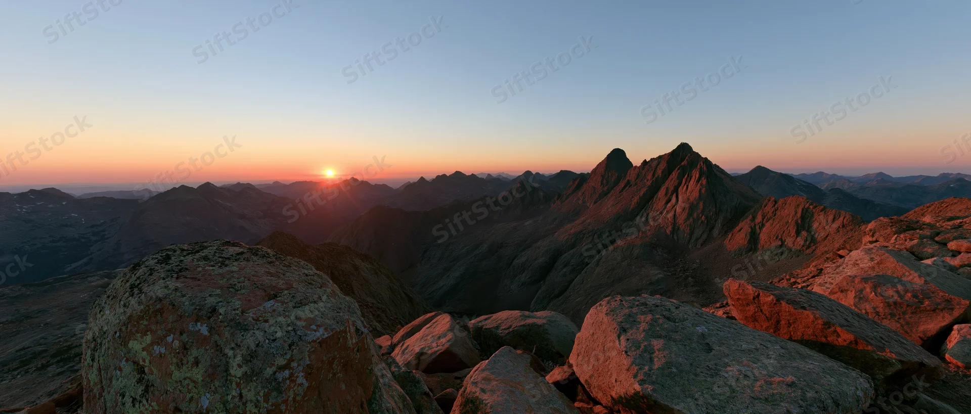 Panoramic view from rocky mountain ridge at sunrise showing jagged peaks and valley below
