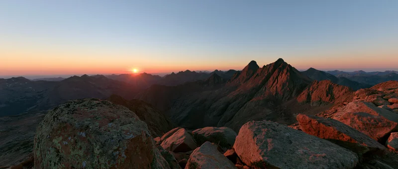 Panoramic view from rocky mountain ridge at sunrise showing jagged peaks and valley below