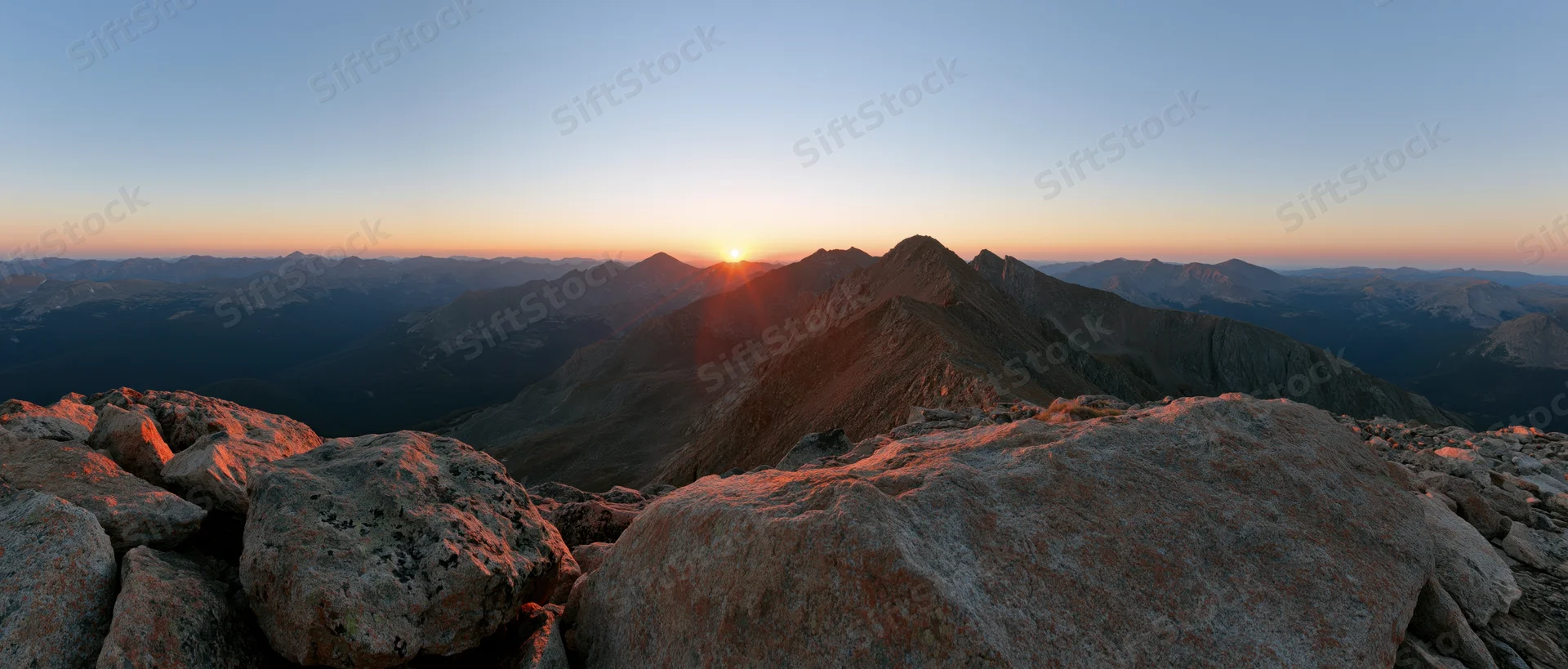 Panoramic view from rocky mountain ridge at sunrise with jagged peaks and valley below
